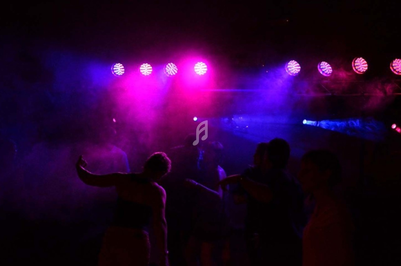 Personnes dansant dans une ambiance sombre avec des lumières colorées violettes et bleues en arrière-plan.