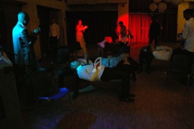 Un homme chante sur scène avec un micro, éclairé par une lumière rouge dans une ambiance de concert.