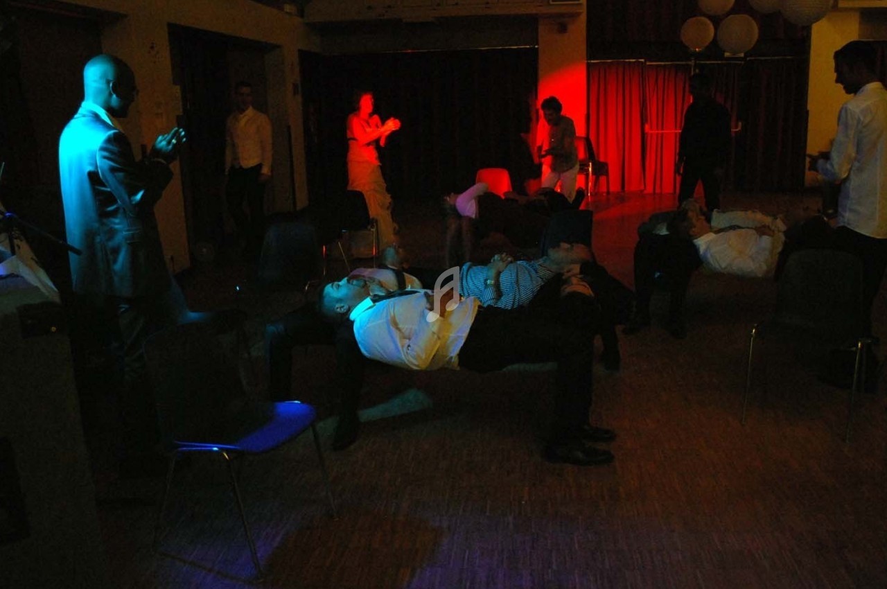 Des personnes allongées sur des chaises dans une salle sombre, éclairée par des lumières colorées.