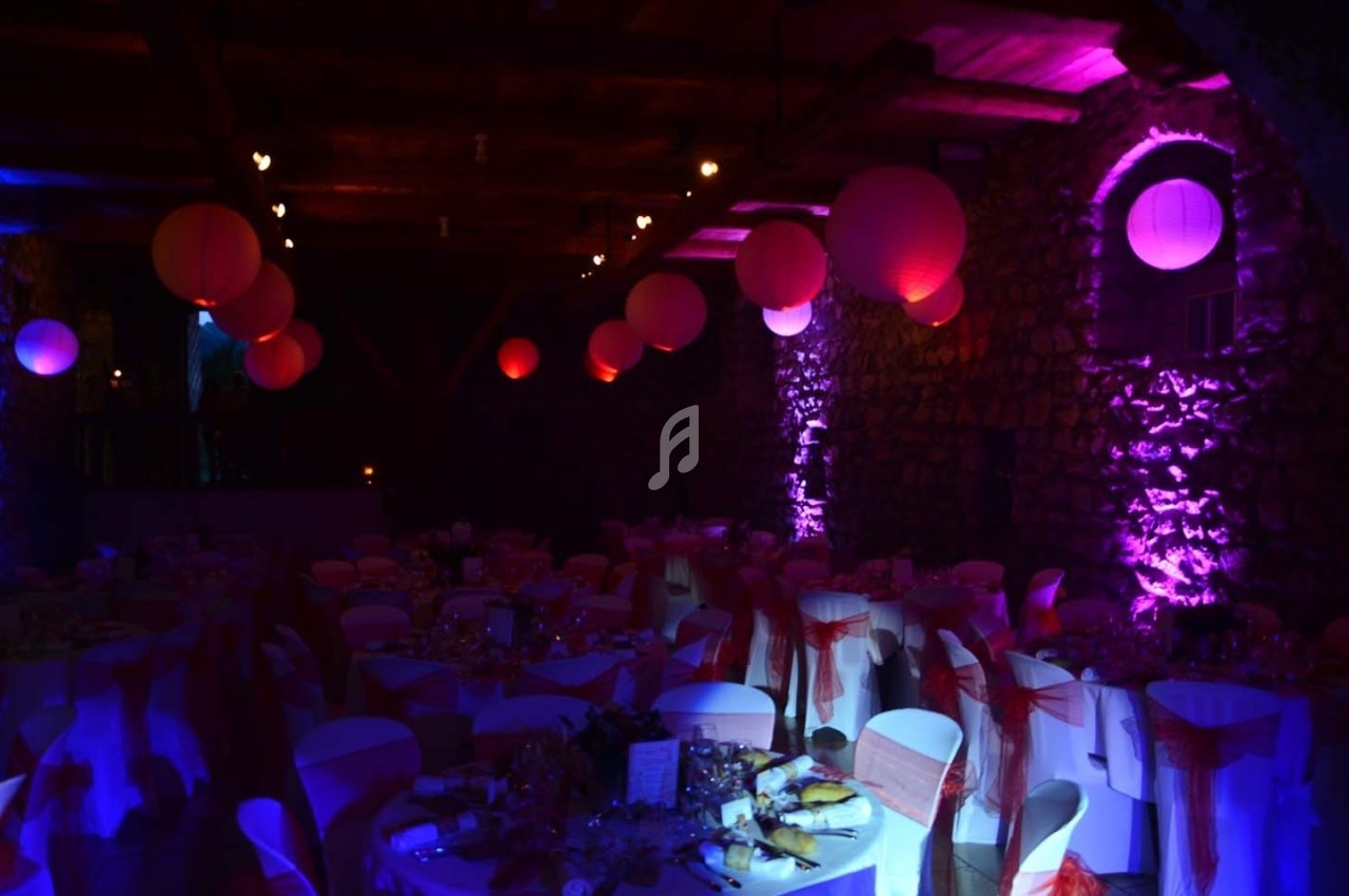 Salle de réception décorée avec des lanternes rouges suspendues, éclairage violet et tables dressées pour un événement.