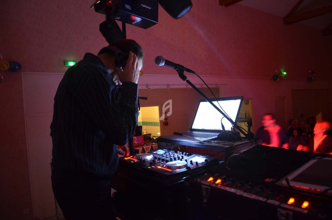 Un DJ mixe de la musique sur une console avec un ordinateur portable dans une salle faiblement éclairée.