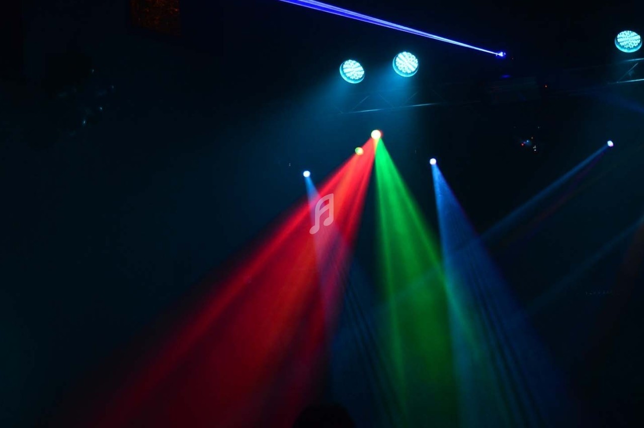 Éclairage de scène avec faisceaux lumineux rouge, vert et bleu sous des projecteurs dans une ambiance sombre.