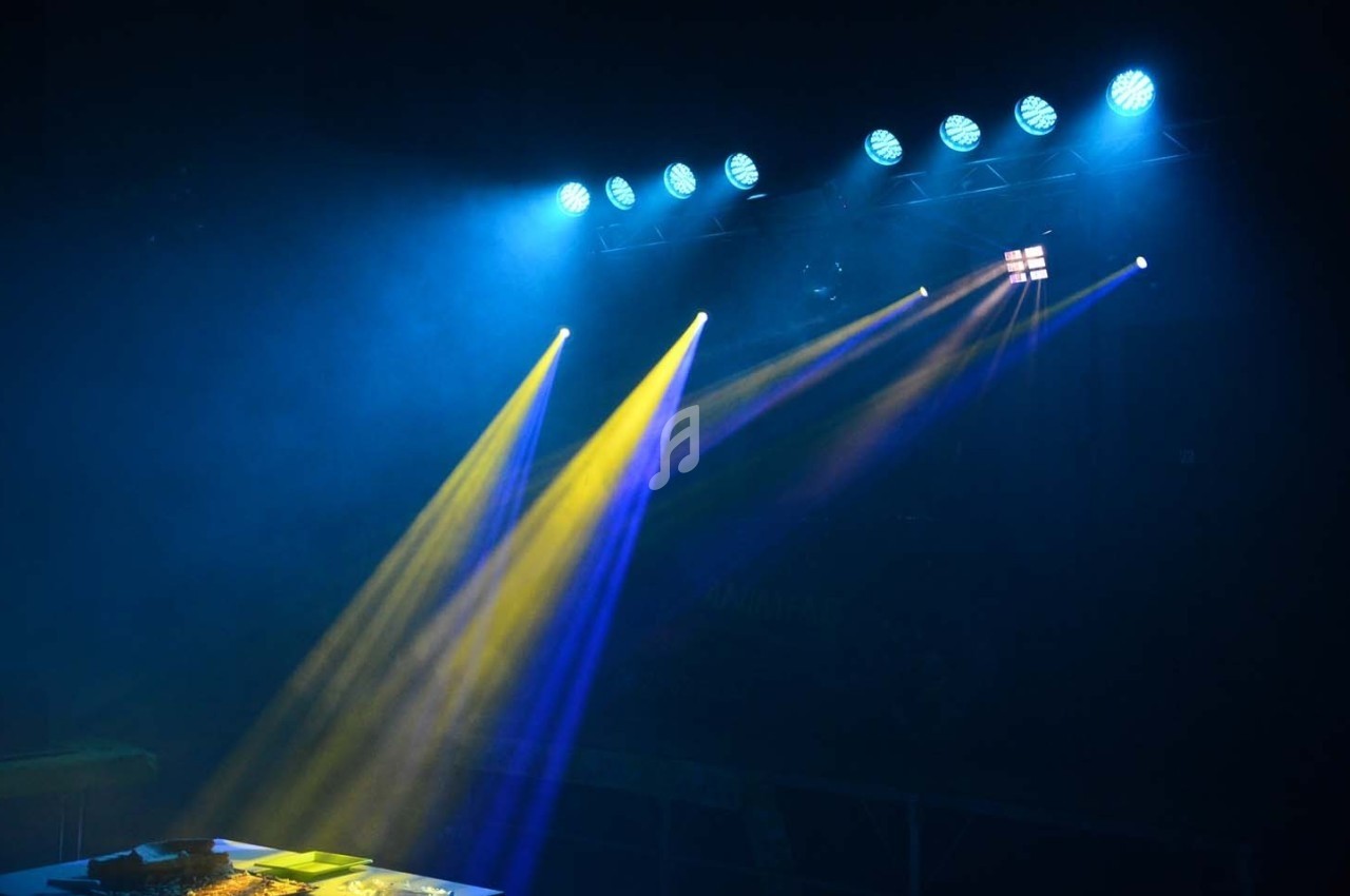 Projecteurs diffusant des faisceaux lumineux jaunes et bleus dans une ambiance sombre avec une scène en arrière-plan.