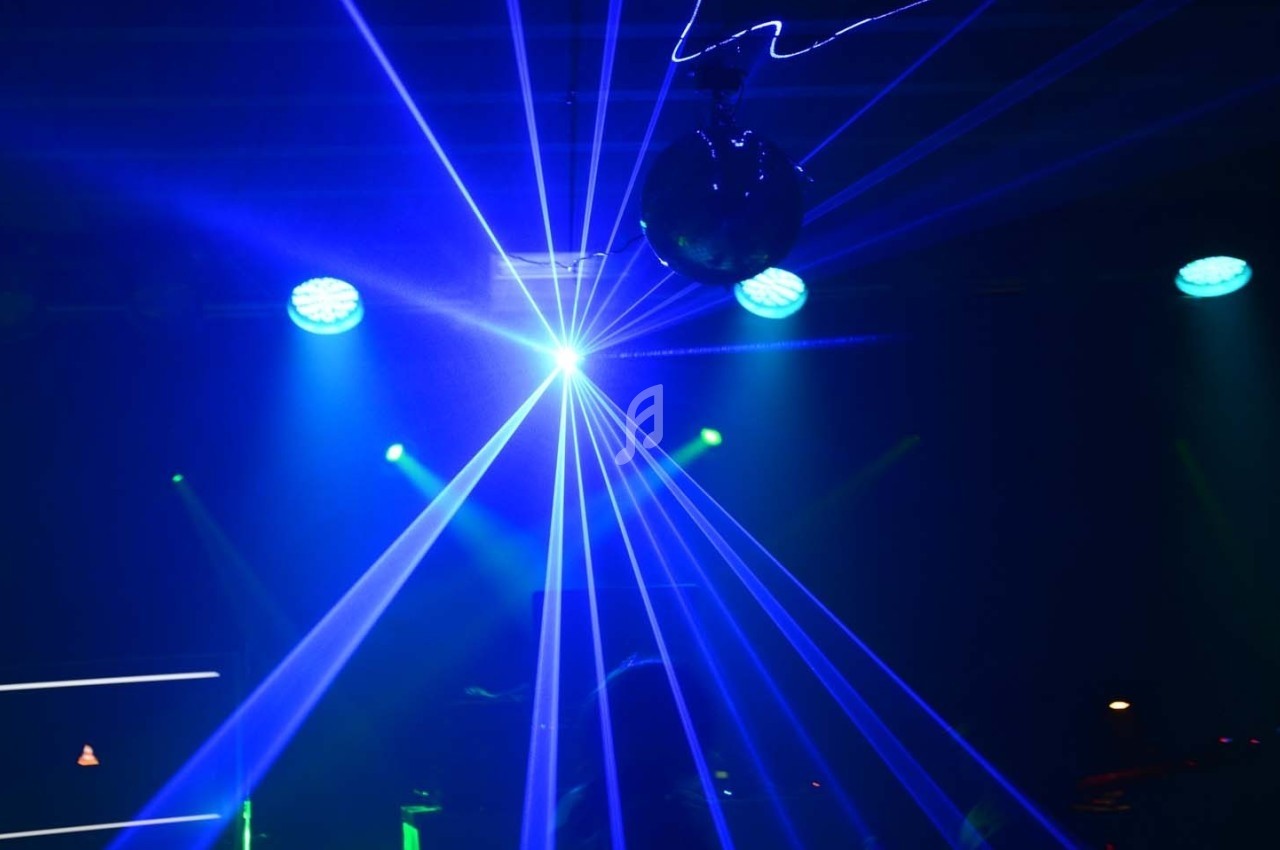 Jeux de lumières bleues et lasers projetés dans une salle sombre avec une boule disco suspendue.