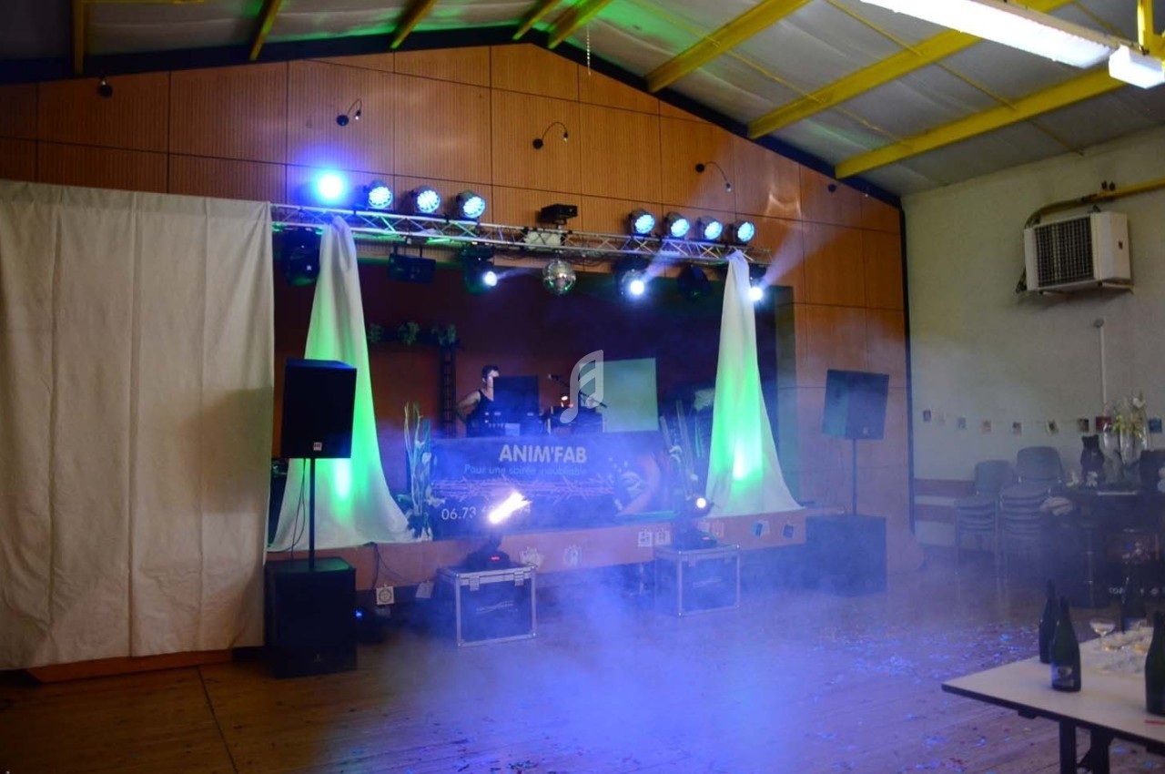 Scène de fête avec jeux de lumières colorées, table en premier plan et équipement de sonorisation sur une estrade.