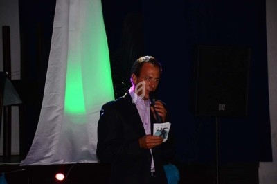 Un homme chante sur scène avec un micro, éclairé par une lumière rouge dans une ambiance de concert.