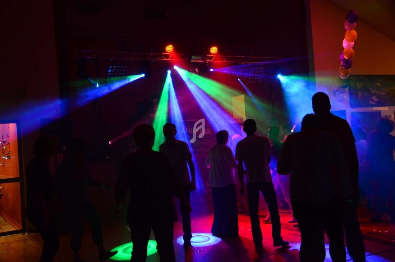 Des personnes dansent dans une salle sombre éclairée par des lumières colorées de projecteurs.