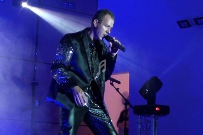 Un homme chante sur scène avec un micro, éclairé par une lumière rouge dans une ambiance de concert.
