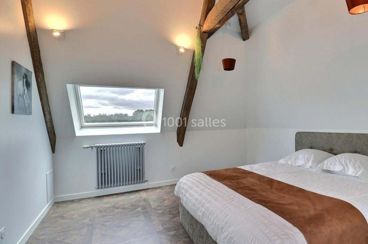 Chambre lumineuse sous combles avec poutres apparentes, lit double, parquet et fenêtre donnant sur un paysage.