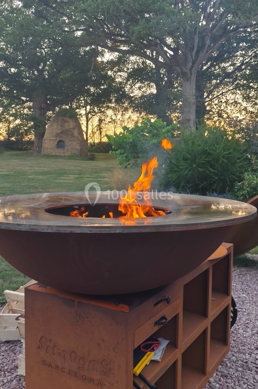Brasero en métal allumé dans un jardin, entouré de végétation et d'arbres au coucher du soleil.