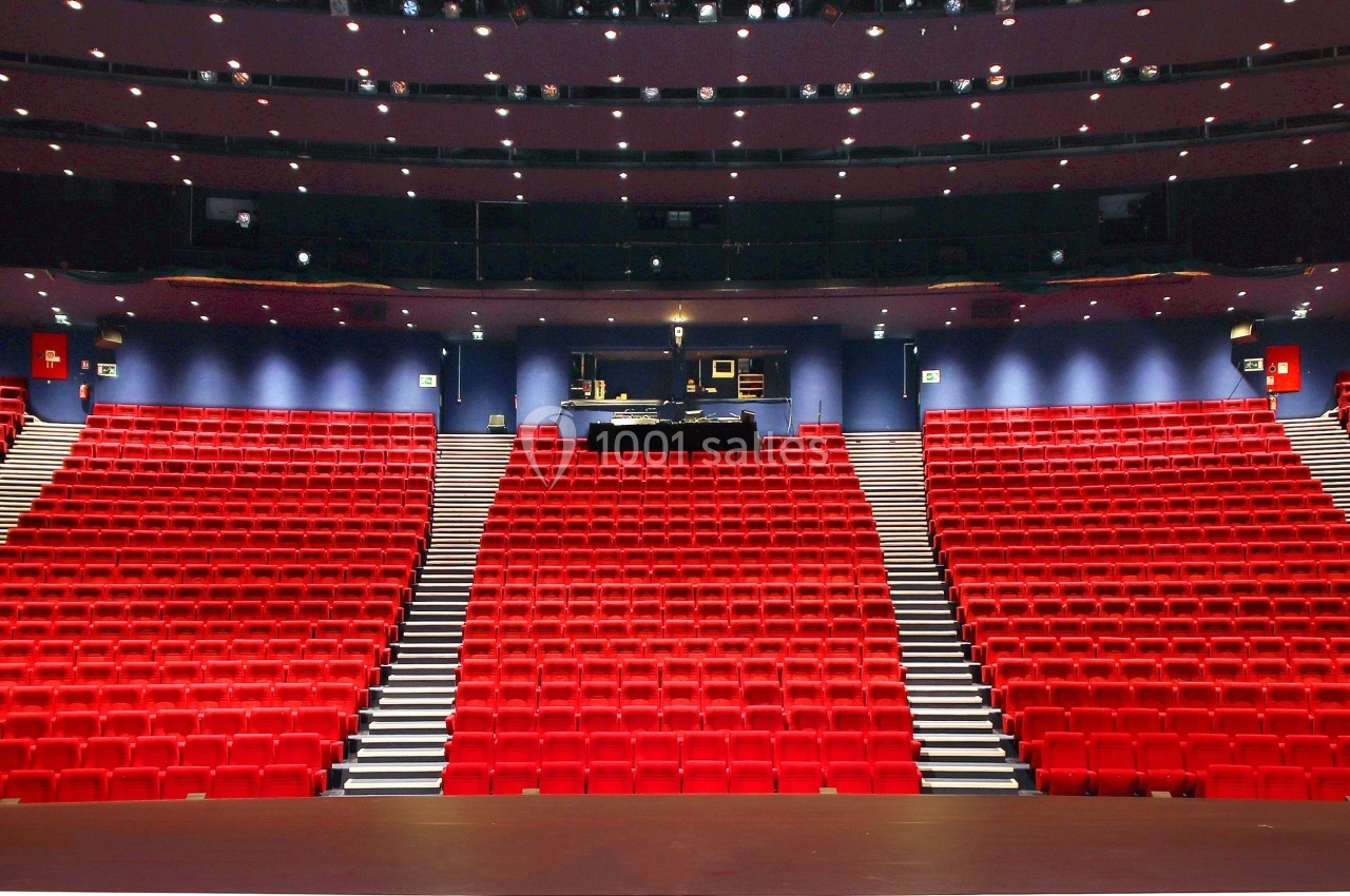 Salle de théâtre vide avec des rangées de sièges rouges et une scène vue depuis le point de vue de l'artiste.