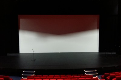 Salle de spectacle vide avec des rangées de sièges violets face à une scène sombre.
