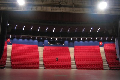 Salle de spectacle vide avec des rangées de sièges violets face à une scène sombre.