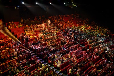 Salle de spectacle vide avec des rangées de sièges violets face à une scène sombre.