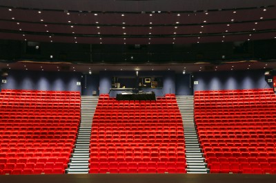 Salle de spectacle vide avec des rangées de sièges violets face à une scène sombre.