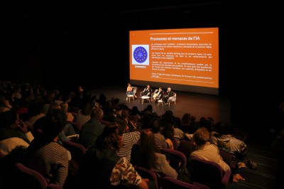 Salle de spectacle vide avec des rangées de sièges violets face à une scène sombre.