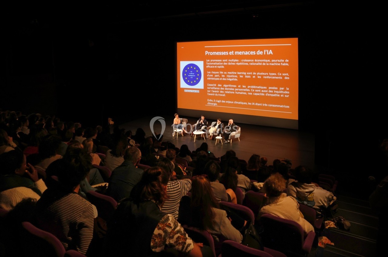 Conférence avec trois intervenants sur scène devant un public, accompagnée d'une présentation projetée sur écran.