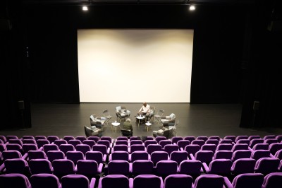 Salle de spectacle vide avec des rangées de sièges violets face à une scène sombre.