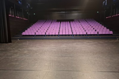 Salle de spectacle vide avec des rangées de sièges violets face à une scène sombre.