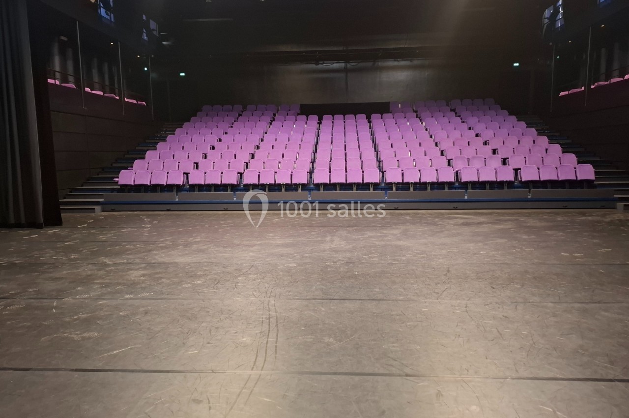 Salle de spectacle vide avec des rangées de sièges violets face à une scène sombre.