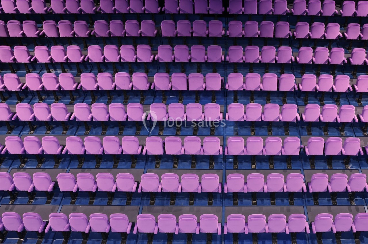 Rangées de sièges violets alignés dans un auditorium vide, vue en plongée.