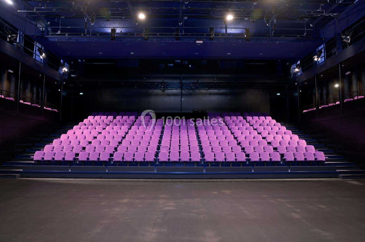 Salle de spectacle vide avec des rangées de sièges violets face à une scène sombre.