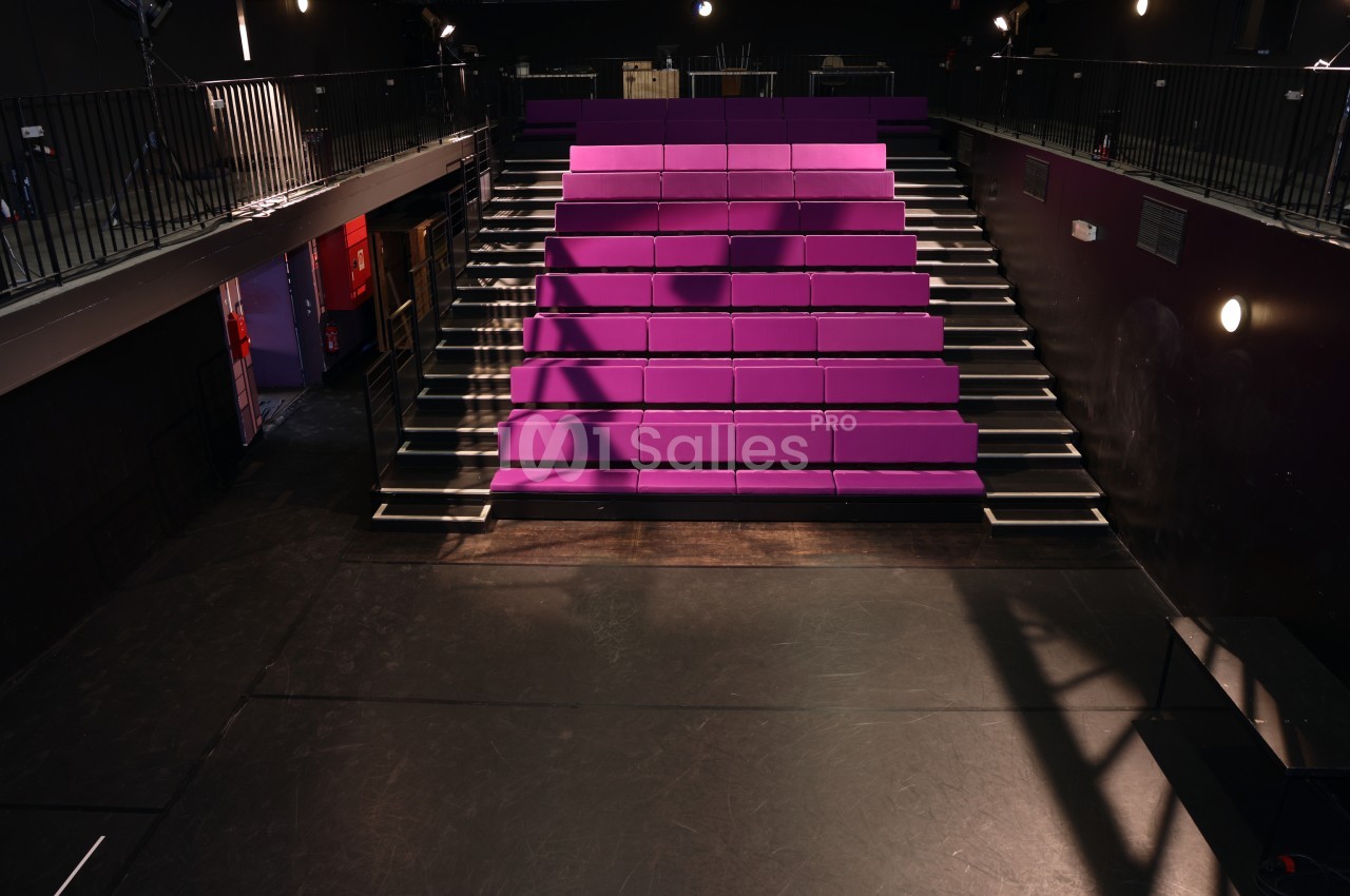 Amphithéâtre avec gradins en fushia éclairés, escaliers noirs et blancs, murs gris, balcons latéraux.
