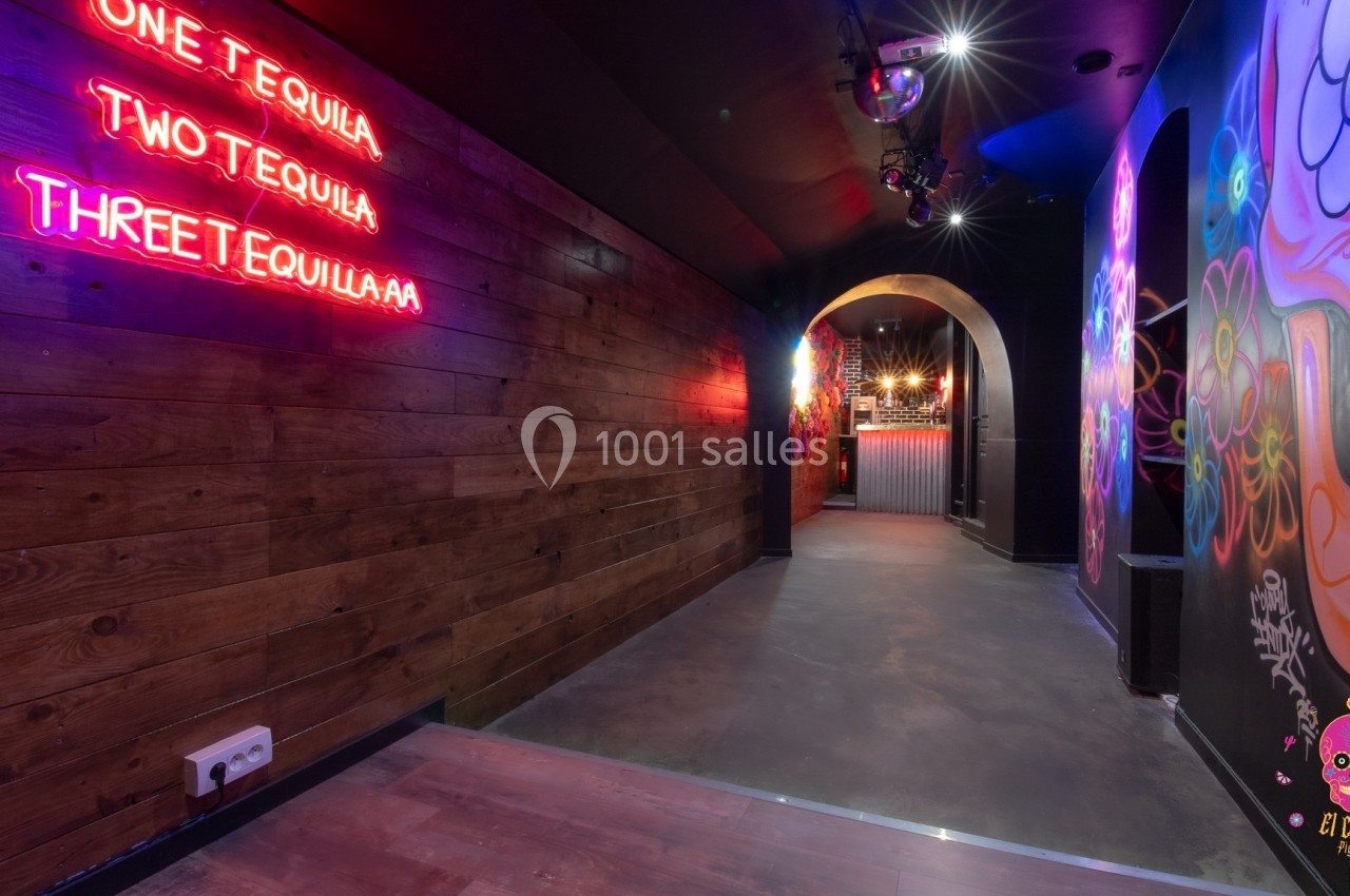 Couloir décoré de fresques colorées et éclairé par des néons roses, menant à un espace avec un bar au fond.