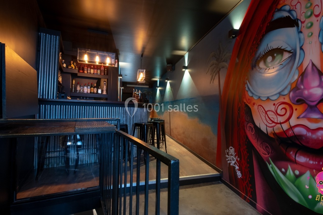 Intérieur d'un bar avec un mur décoré d'une fresque colorée représentant un visage, éclairage tamisé.
