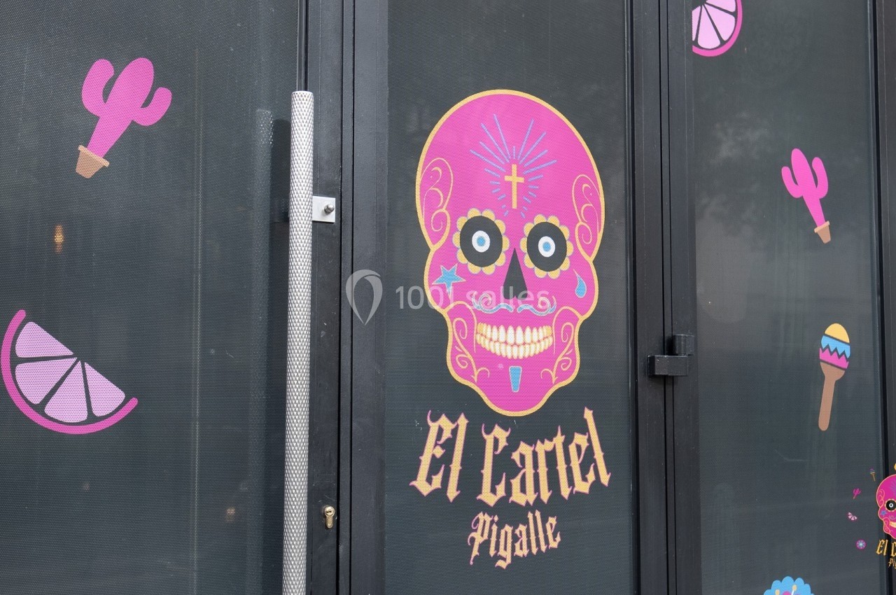 Autocollants colorés de motifs mexicains sur une porte vitrée, avec un crâne rose et l'inscription ’El Cartel Pigalle’.