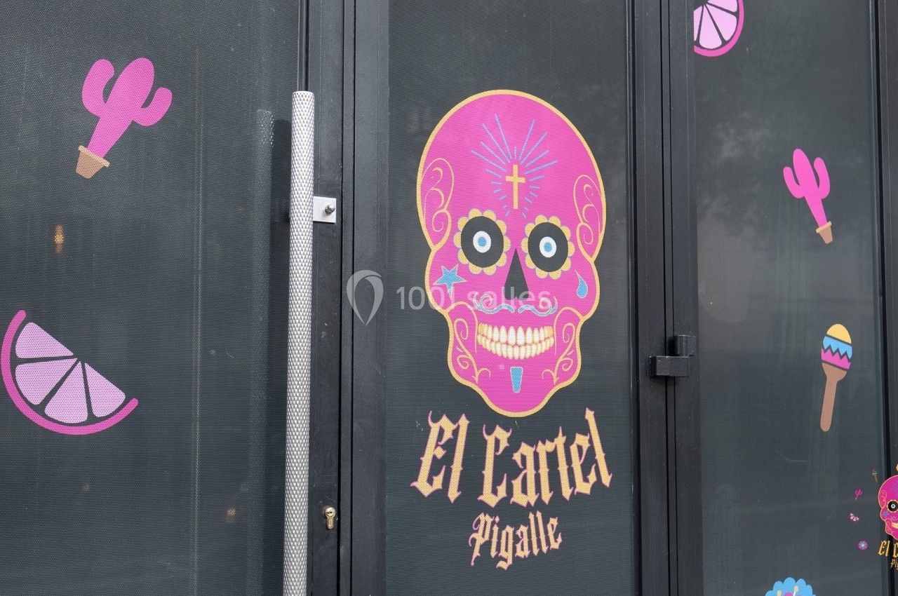 Autocollants colorés de motifs mexicains sur une porte vitrée, avec un crâne rose et l'inscription ’El Cartel Pigalle’.