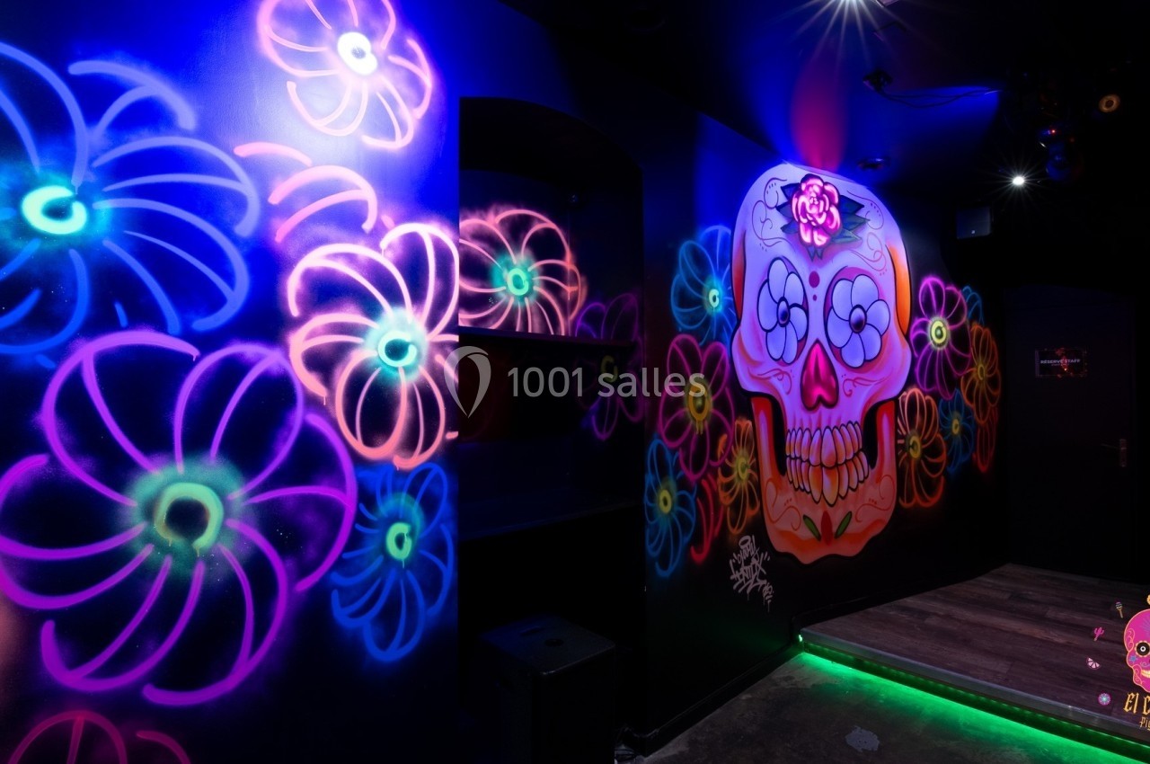 Mur décoré de graffitis colorés représentant des fleurs et un crâne stylisé, éclairé par des lumières néon.