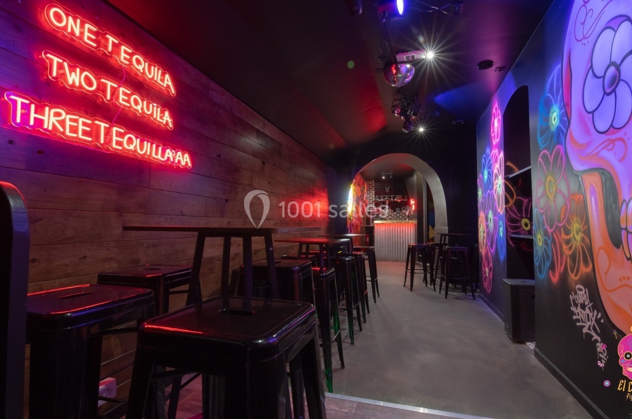 Bar avec des murs décorés de graffitis colorés, éclairage néon et tabourets hauts alignés près de tables.