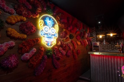 Autocollants colorés de motifs mexicains sur une porte vitrée, avec un crâne rose et l'inscription ’El Cartel Pigalle’.