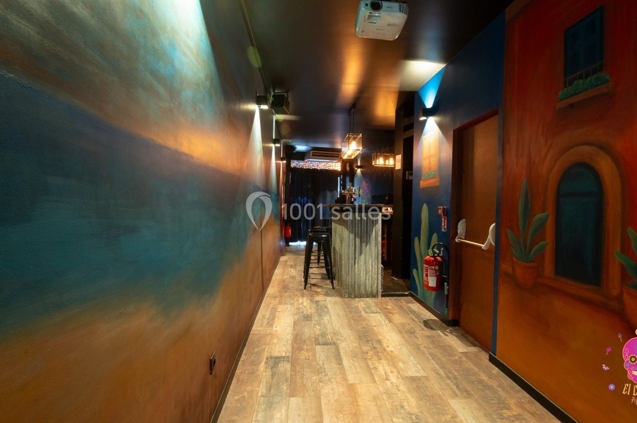 Couloir étroit avec murs peints aux tons chauds menant à un bar éclairé, décoré dans un style chaleureux.