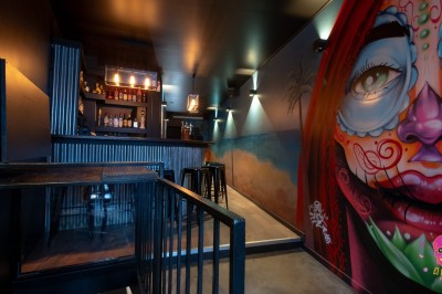 Autocollants colorés de motifs mexicains sur une porte vitrée, avec un crâne rose et l'inscription ’El Cartel Pigalle’.