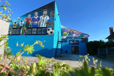 Terrain de pétanque intérieur avec sol en sable, encadré de murs en tôle et briques, à côté d'un espace détente.