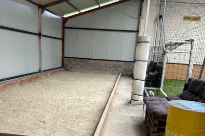 Terrain de pétanque intérieur avec sol en sable, encadré de murs en tôle et briques, à côté d'un espace détente.