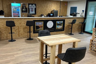 Terrain de pétanque intérieur avec sol en sable, encadré de murs en tôle et briques, à côté d'un espace détente.