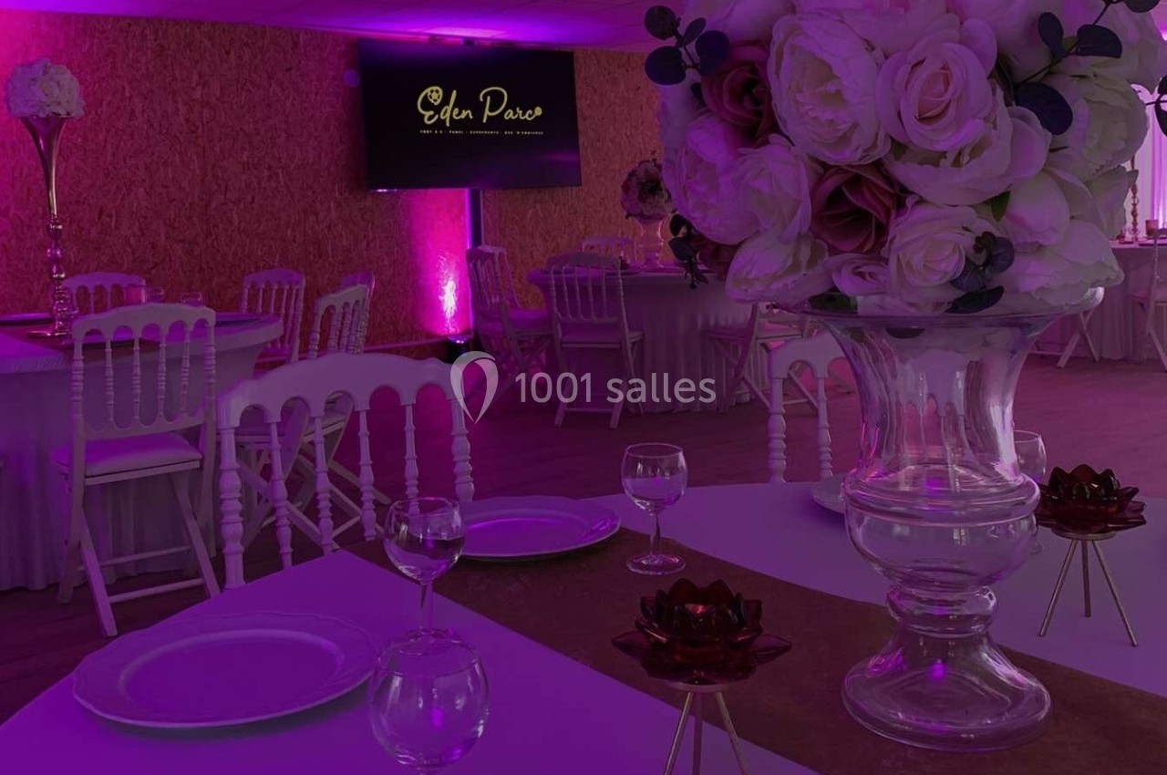 Salle de réception décorée avec des tables dressées, un grand bouquet de fleurs et un éclairage rose.