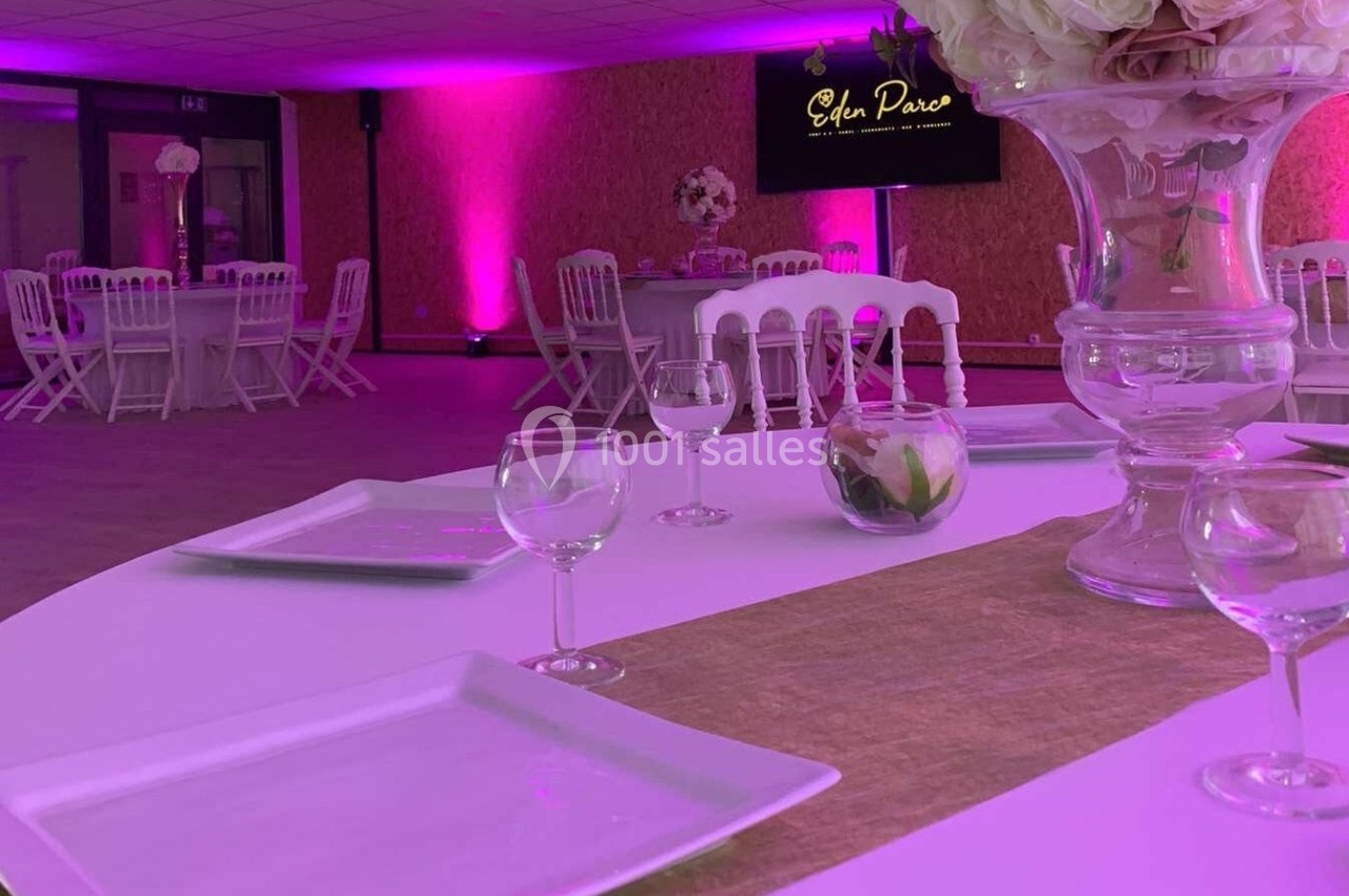Salle de réception décorée avec des tables dressées, éclairage rose et écran affichant ’Eden Parc’.