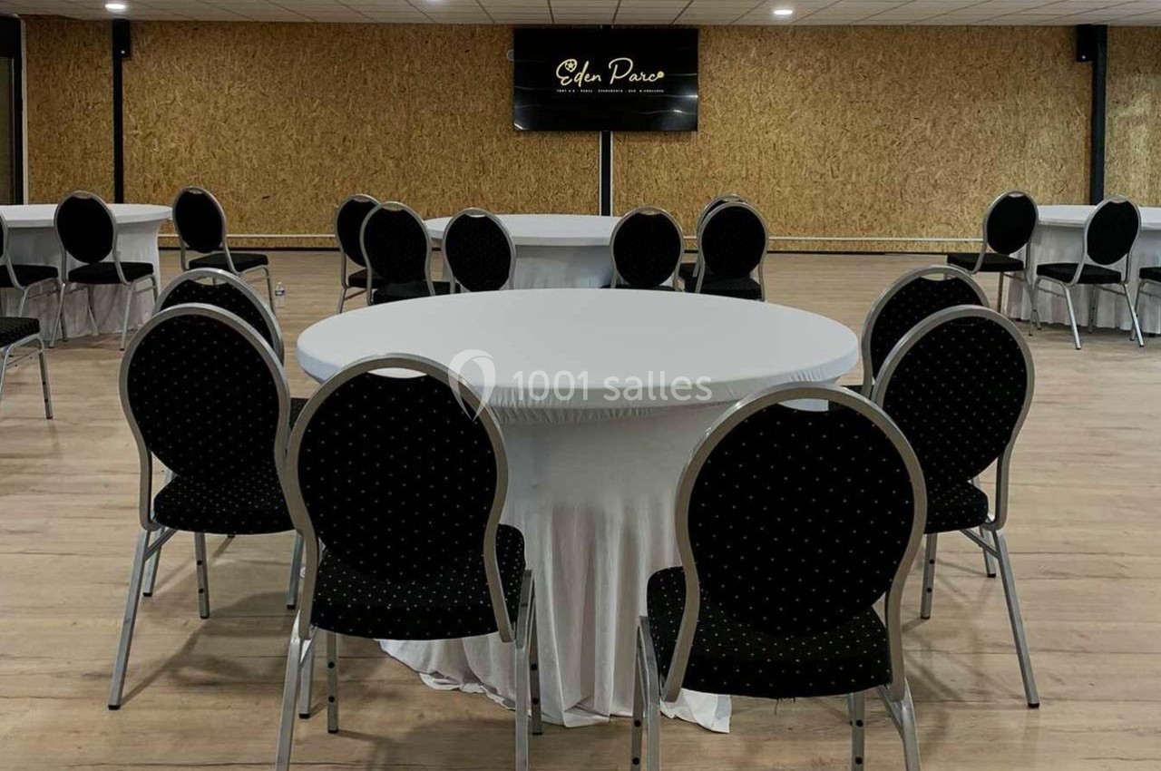 Salle avec des tables rondes recouvertes de nappes blanches et des chaises noires à motifs, sol en bois clair.