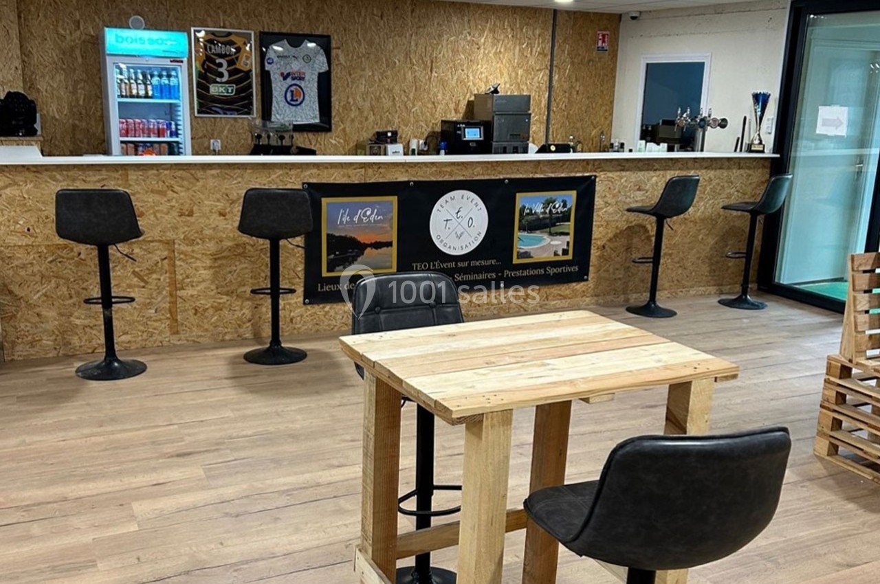 Un espace intérieur avec un comptoir en bois, des tabourets hauts, une table en bois et un sol en parquet clair.