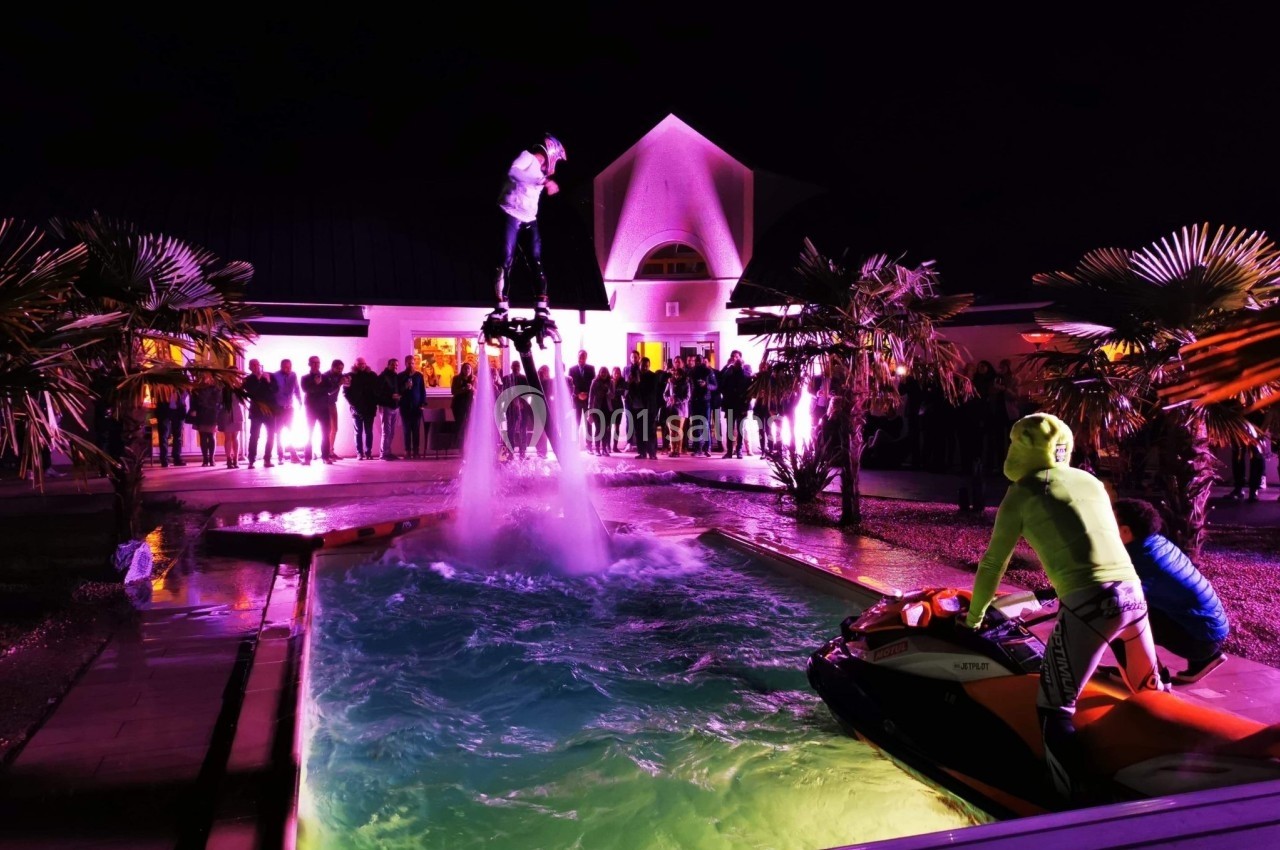 Un homme sur un flyboard au-dessus d'une piscine, entouré d'un public et éclairé par des lumières colorées la nuit.