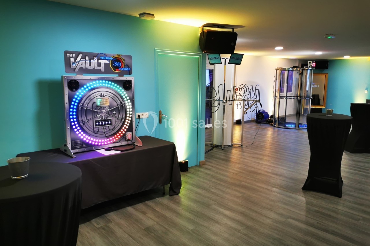 Salle avec un jeu interactif lumineux sur une table, des tables hautes noires et un décor moderne aux tons bleus.