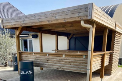 Piscine éclairée de nuit avec des lumières rouges et violettes, entourée de palmiers et d'une table avec un verre.