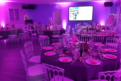 Piscine éclairée de nuit avec des lumières rouges et violettes, entourée de palmiers et d'une table avec un verre.