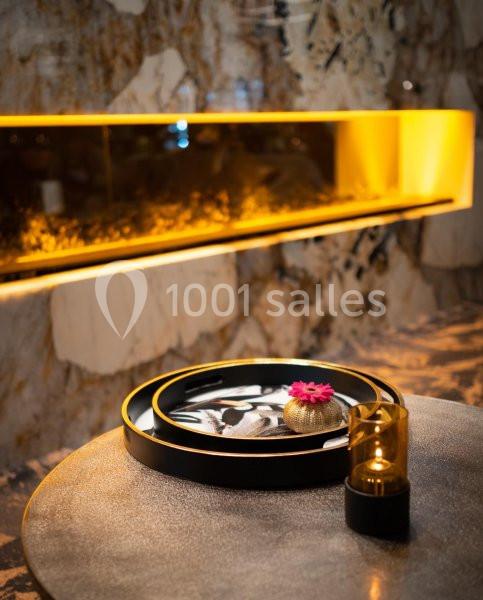 Plateau décoratif noir avec une fleur rose et une bougie, posé sur une table devant un mur en marbre éclairé.