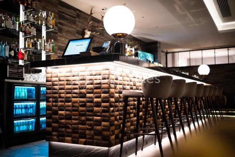 Bar moderne avec comptoir éclairé, tabourets hauts, étagères de bouteilles et ambiance lumineuse tamisée.