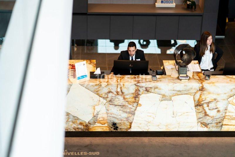 Accueil d'un hôtel avec un comptoir en marbre, un réceptionniste et une employée en arrière-plan.